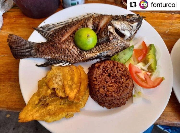 Plato típico del Caribe colombiano con pescado frito entero, arroz de coco, patacones y ensalada de tomate y aguacate.