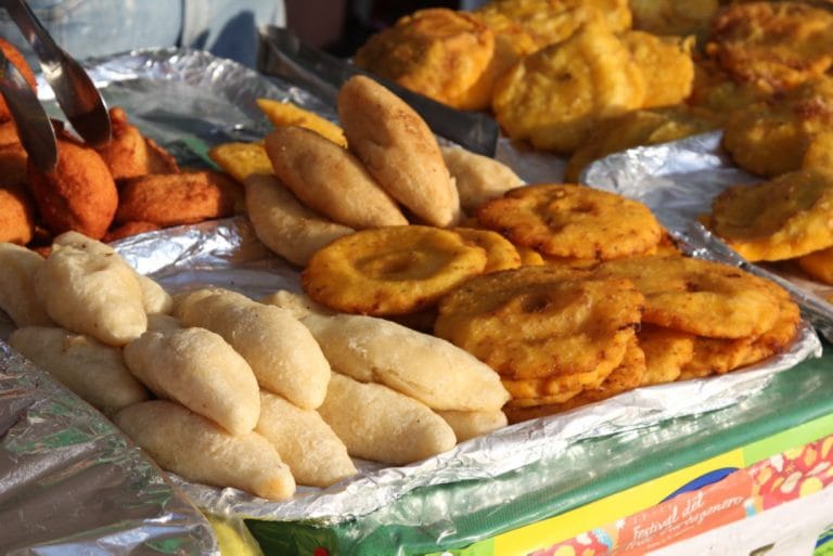 Bandeja con frituras típicas del Caribe colombiano: deditos de yuca, arepas de maíz fritas y patacones dorados en un puesto de mercado.