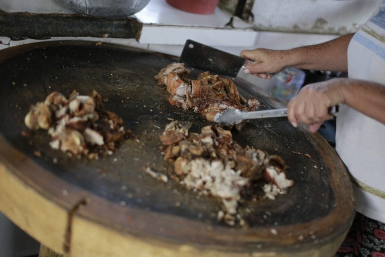 Cocinera troceando carne asada sobre un budare de barro en una cocina tradicional del Caribe colombiano.